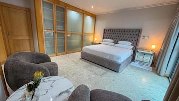 Um quarto com uma cama, guarda-roupa, área de estar e uma pequena mesa com um vaso.