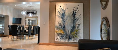 Un interior moderno con zona de comedor, un cuadro abstracto grande y una sala de estar con una mesa de centro.