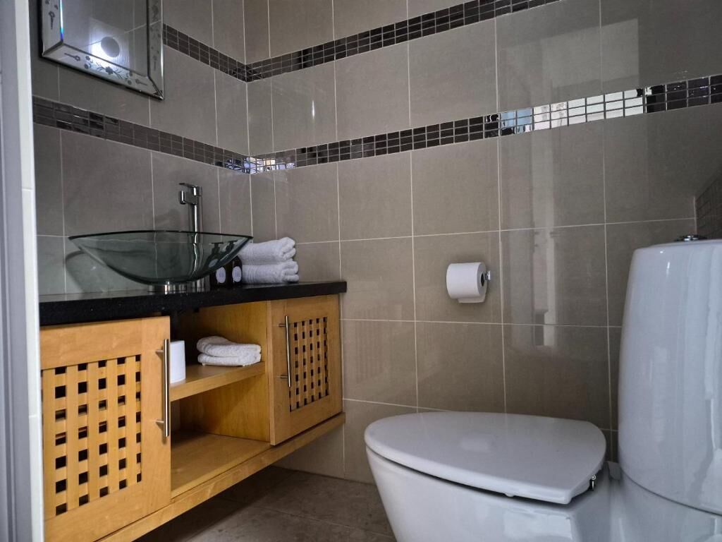 Un baño con inodoro, lavamanos de vidrio y espejo.