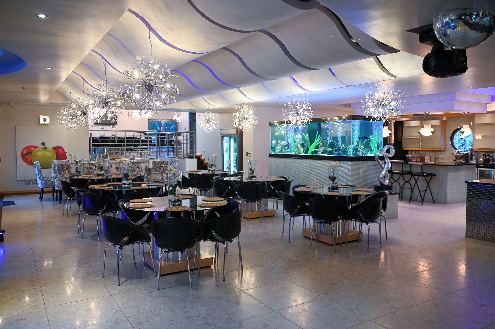 A spacious indoor area with multiple dining tables and chairs, a large aquarium, and modern ceiling design.