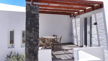 Un patio con mesa y sillas, un pilar de piedra y una pérgola de madera.
