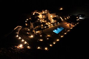 Vista nocturna de un resort con varias edificaciones, piscina e iluminación exterior.