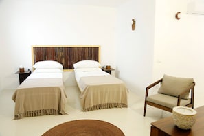 A hotel room with two beds, a wooden headboard, a chair, and a small table with a decorative bowl.