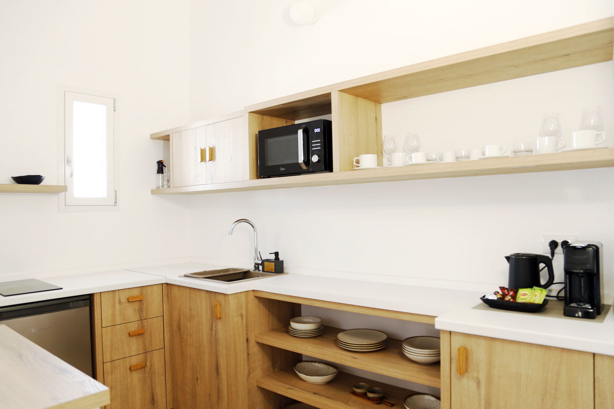 A modern kitchen with white countertops, wooden cabinets, a built-in microwave, and a coffee maker.