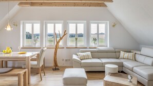 A modern living room with a wooden ceiling, a white sofa, a dining table with chairs, and large windows with a view of the countryside. - Villa 'Ferienhaus Residenz am Vulkanradweg' with Terrace, Garden & Wi-Fi (Grebenhain)