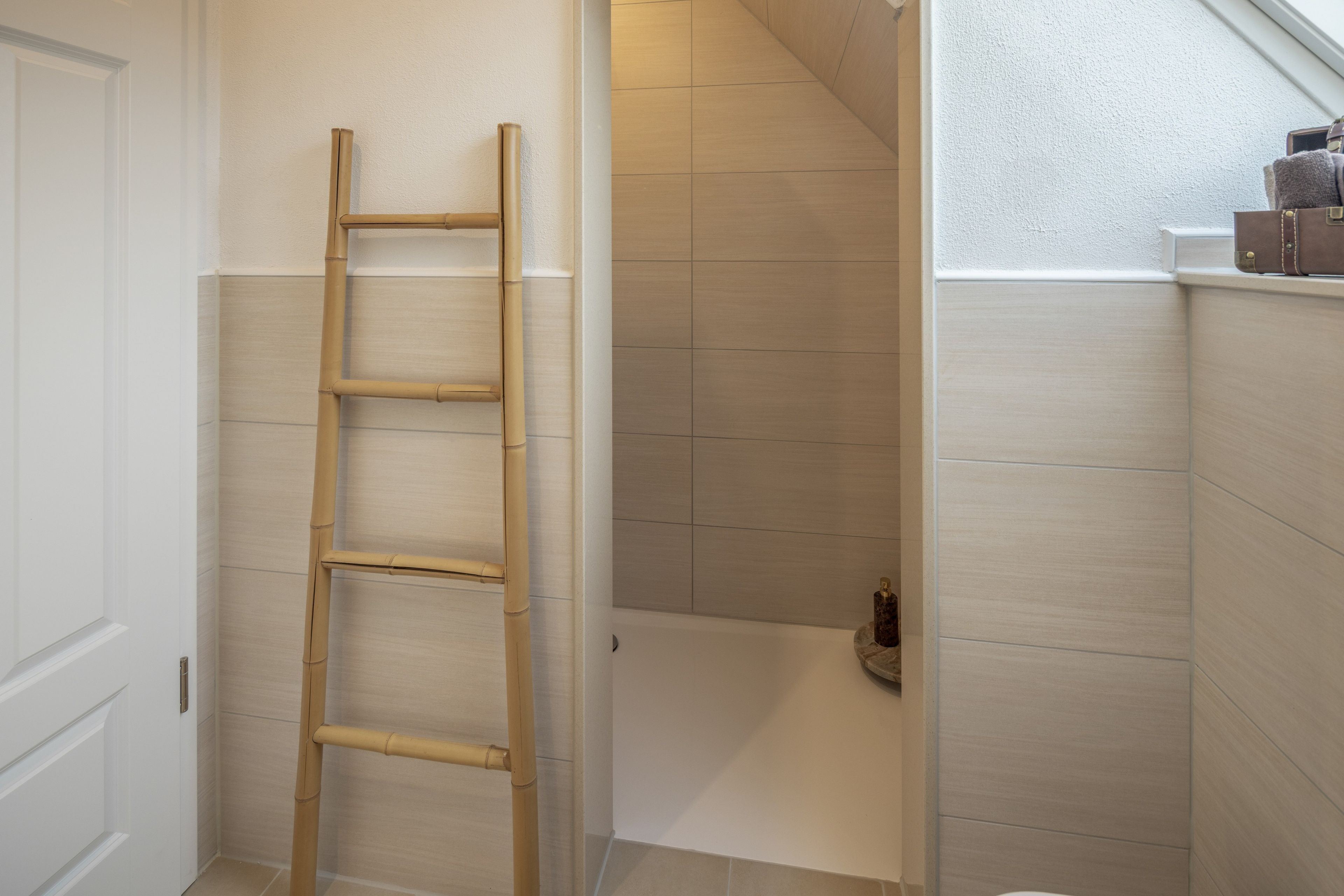 A bathroom with a wooden ladder, a bathtub, and a small shelf with toiletries.
