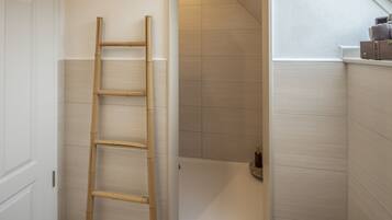 A bathroom with a wooden ladder, a bathtub, and a small shelf with toiletries.