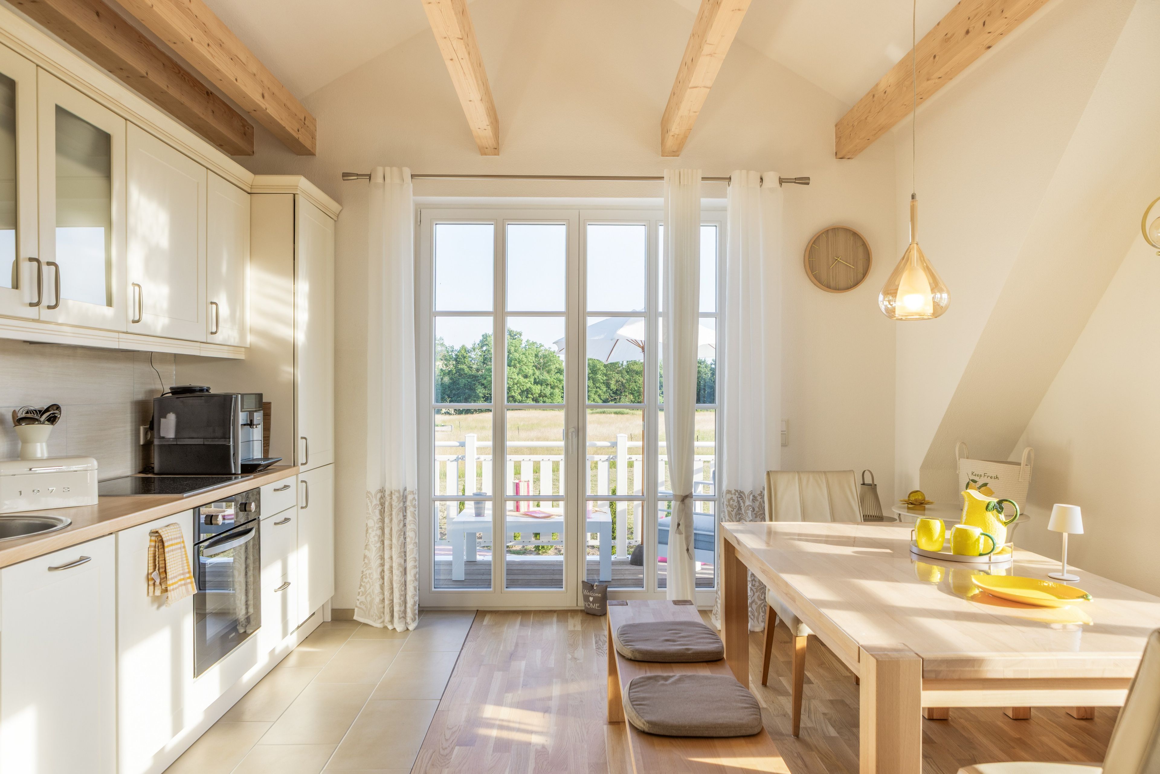 A kitchen with white cabinets, a coffee machine, and a view to an outdoor deck.
