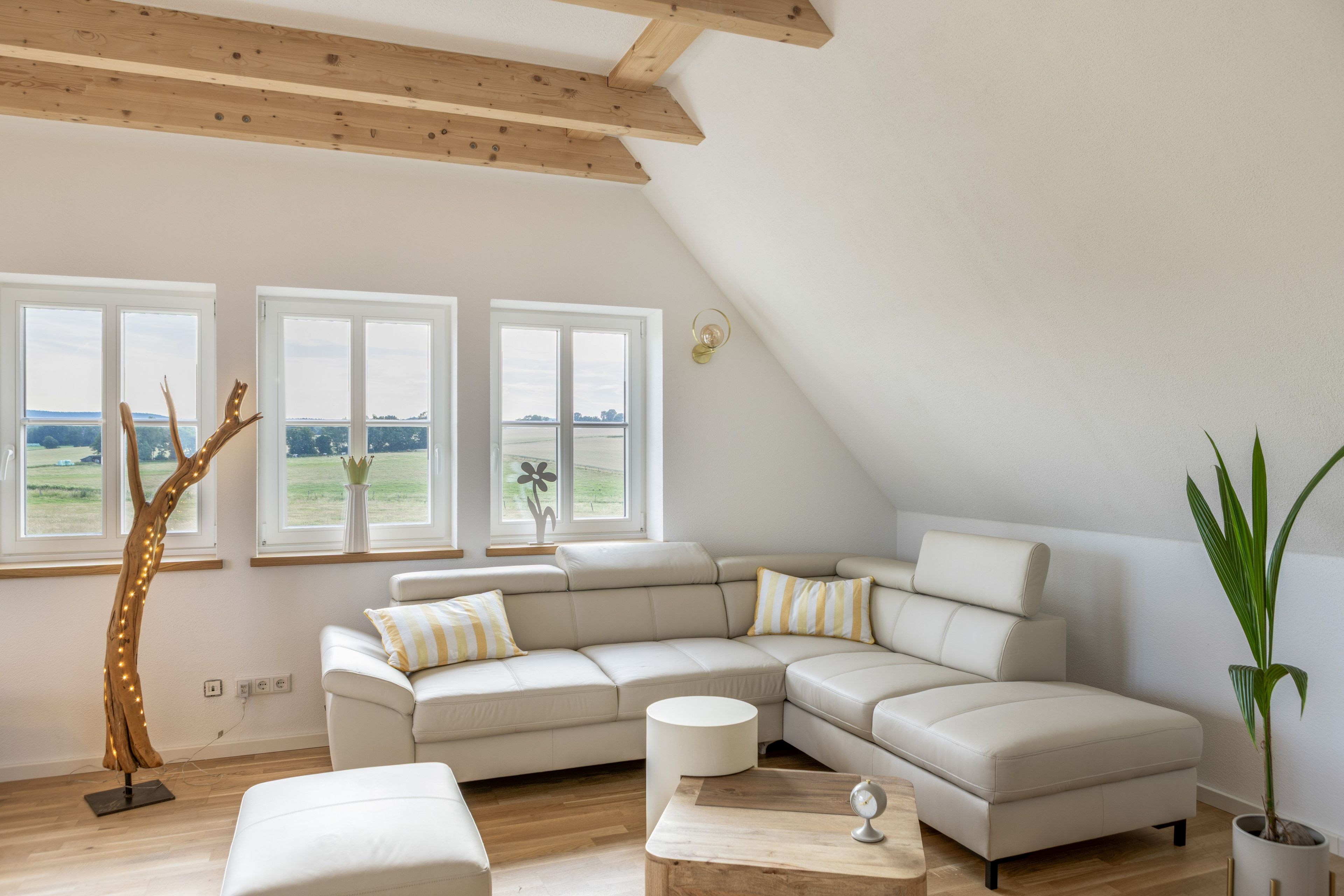 A modern living room with a sectional sofa, a wooden floor, and large windows offering a view of the outdoors.