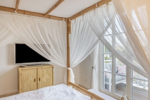 A room with a bed, a television on a cabinet, and a window with a view of the outside.