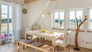 A modern kitchen with a wooden table, white chairs, and a bench. There is a window with a view of the outdoors. - Villa 'Ferienhaus Residenz am Vulkanradweg' with Terrace, Garden & Wi-Fi (Grebenhain)