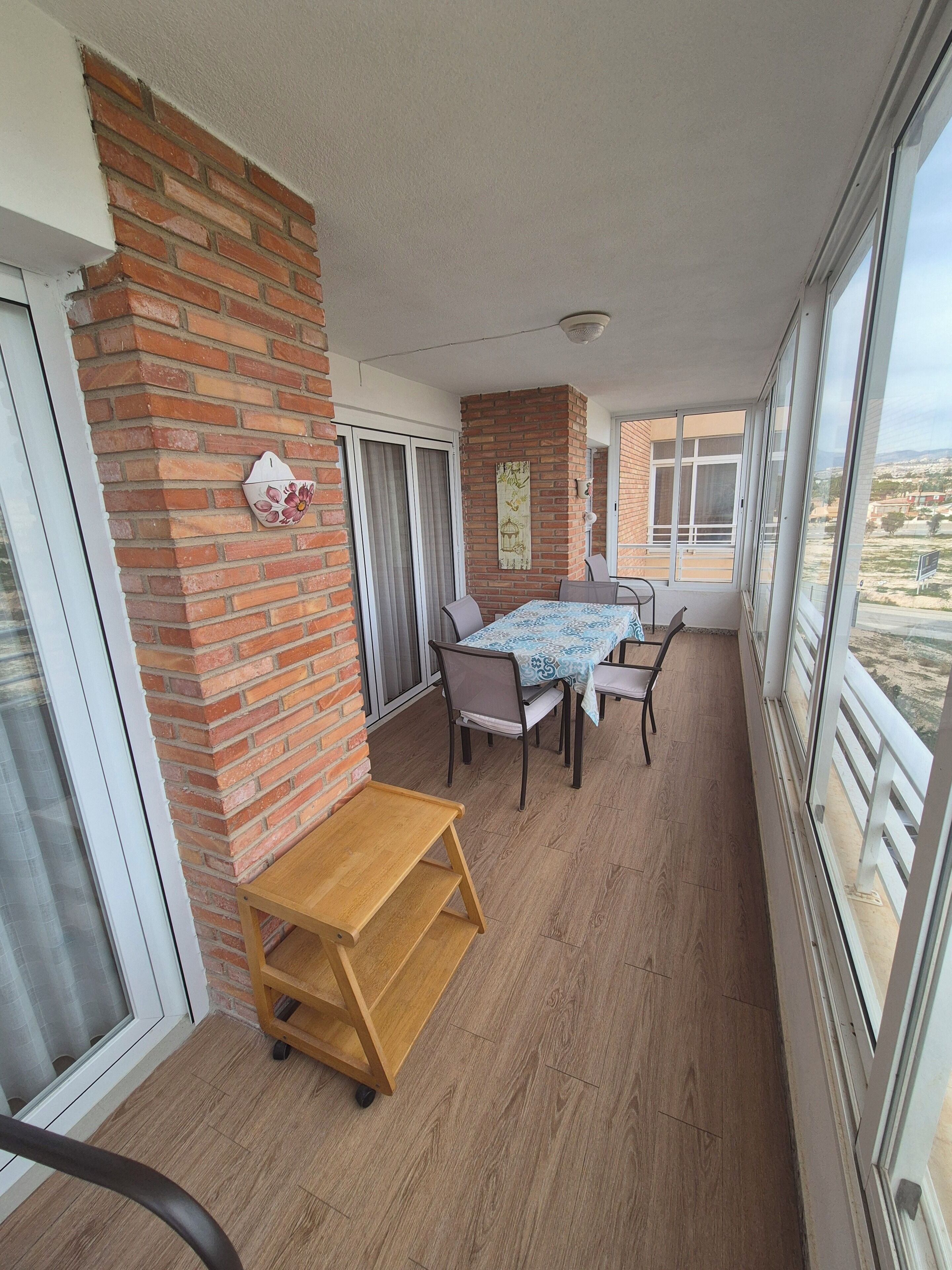 A balcony with a table and chairs, a wooden bench, a brick wall, and a view of the landscape.