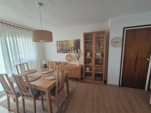 A dining area with a wooden table and chairs, a cabinet with glass doors, and a painting on the wall. - Vacation Rental Apartment Near the Beach (VC)