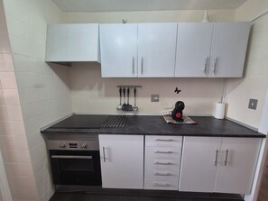 A compact kitchen with white cabinets, a black countertop, and a built-in oven. - Vacation Rental Apartment Near the Beach (VC)