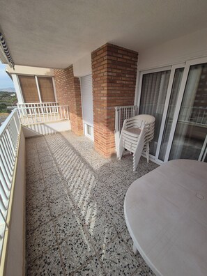 A balcony with a tiled floor, a brick wall, and a white railing. - Vacation Rental Apartment Near the Beach (VC)