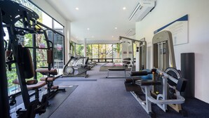 A gym with various exercise equipment, large windows, and an air conditioning unit.