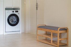 Een wasruimte met een Samsung wasmachine, een houten bankje en een betegelde muur.