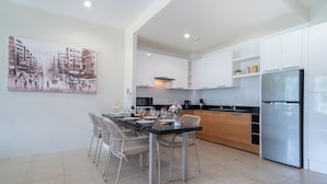 A modern kitchen with white cabinetry, a stainless steel refrigerator, and a dining area with a table set for four.