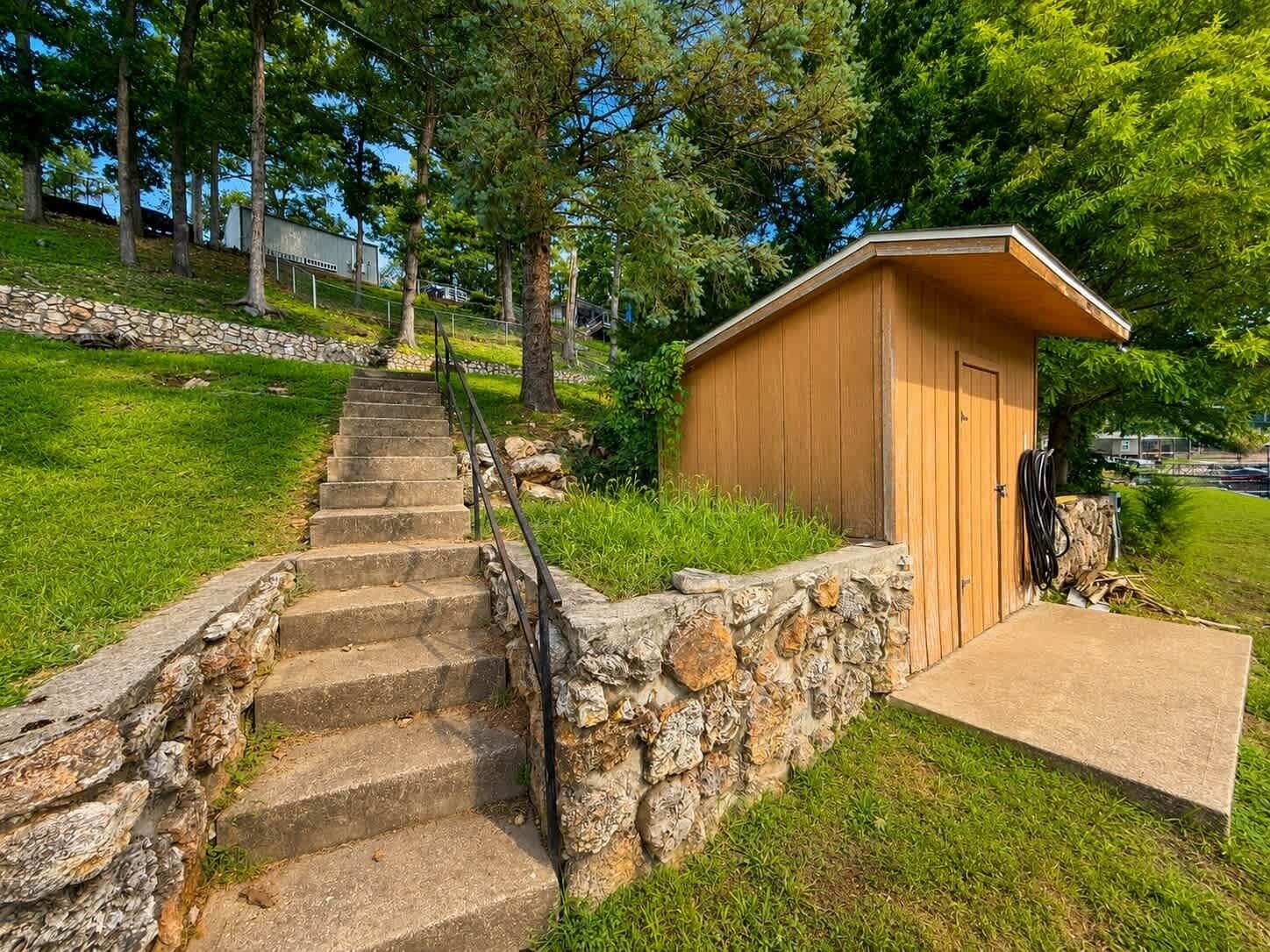 A wooden cabin with a stone staircase leading up to it, surrounded by greenery and trees.