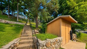 Una cabaña de madera con una escalera de piedra que lleva a ella, rodeada de follaje y árboles.