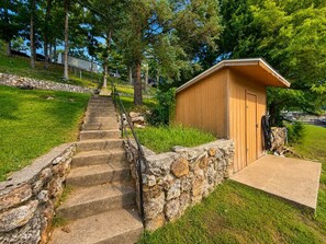 Un cobertizo de madera con una puerta, un muro de piedra y una escalera de concreto que lleva a él.