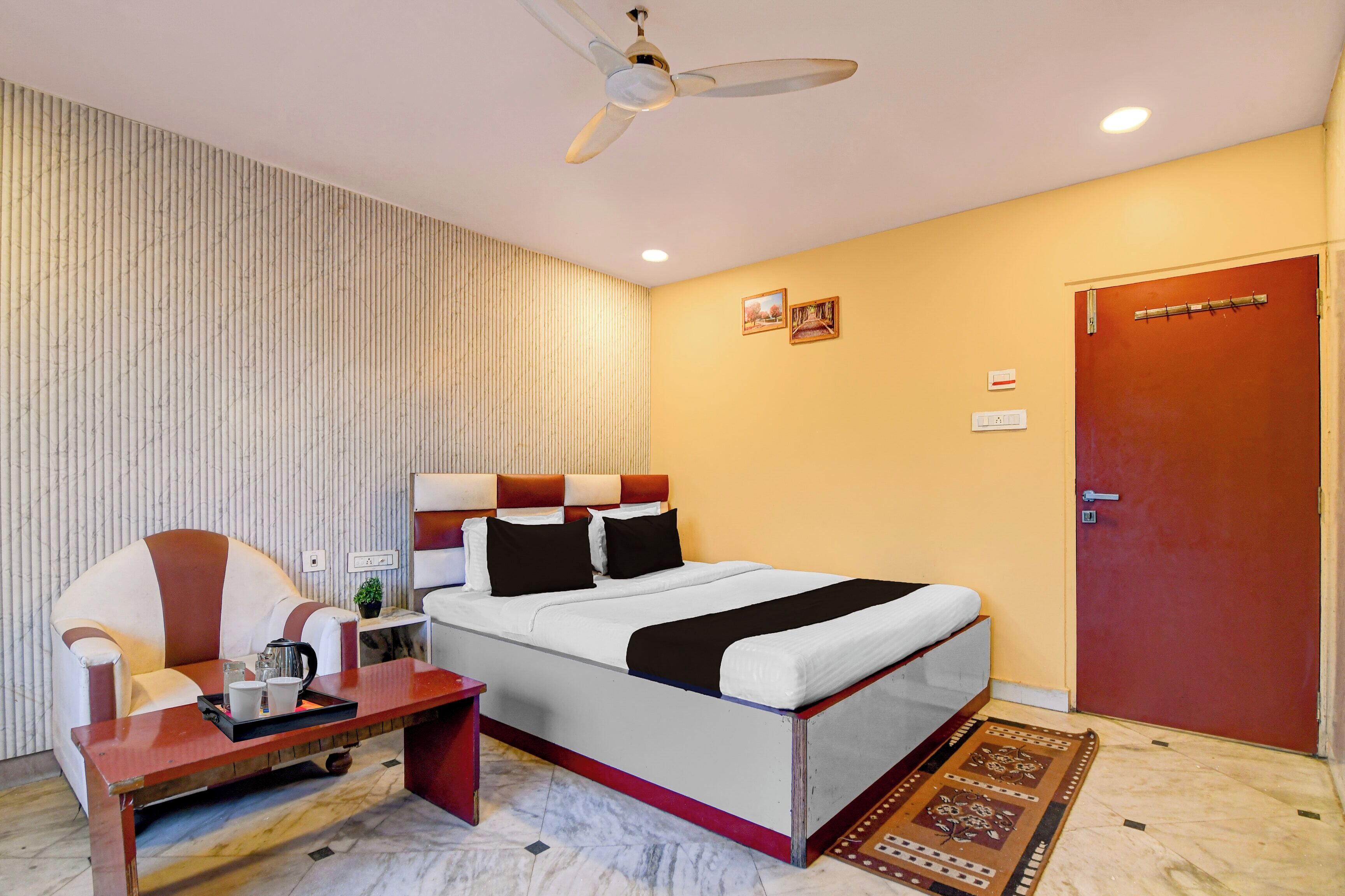 A hotel room with a bed, a desk, a chair, a ceiling fan, and a door.