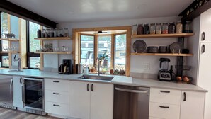 A modern kitchen with stainless steel appliances, wooden shelves, and a view through the window. - Lofted home in a quiet neighborhood of downtown Salida. California king bed plus super comfortable queen murphy bed and FullXL floor mattress in loft. Two levels, two bathrooms, beautifully landscaped private courtyard with hot tub and gas fire pit. (Salida)