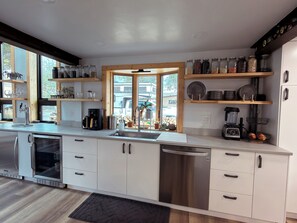 Eine moderne Küche mit Edelstahlgeräten, Holzregalen und Blick durch das Fenster.