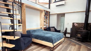 A loft-style bedroom with a bed, a chair, a bookshelf, and a fireplace. - Lofted home in a quiet neighborhood of downtown Salida. California king bed plus super comfortable queen murphy bed and FullXL floor mattress in loft. Two levels, two bathrooms, beautifully landscaped private courtyard with hot tub and gas fire pit. (Salida)