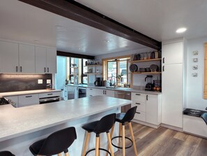 A modern kitchen with white cabinets, a central island with bar stools, and a wooden ceiling beam. - Lofted home in a quiet neighborhood of downtown Salida. California king bed plus super comfortable queen murphy bed and FullXL floor mattress in loft. Two levels, two bathrooms, beautifully landscaped private courtyard with hot tub and gas fire pit. (Salida)