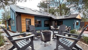 A modern outdoor seating area with Adirondack chairs and a central table, surrounded by a building with a metal roof and wooden accents. - Lofted home in a quiet neighborhood of downtown Salida. California king bed plus super comfortable queen murphy bed and FullXL floor mattress in loft. Two levels, two bathrooms, beautifully landscaped private courtyard with hot tub and gas fire pit. (Salida)