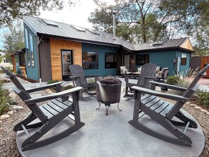 Ein moderner Außenbereich mit Adirondack-Stühlen und einem zentralen Tisch, umgeben von einem Gebäude mit Metallverkleidung und Holzapplikationen.