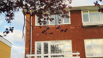 A two-story brick building with a white balcony, a 'NO PARKING OR WAITING BY ORDER OF THE MANAGING AGENTS' sign, and a grassy front yard.