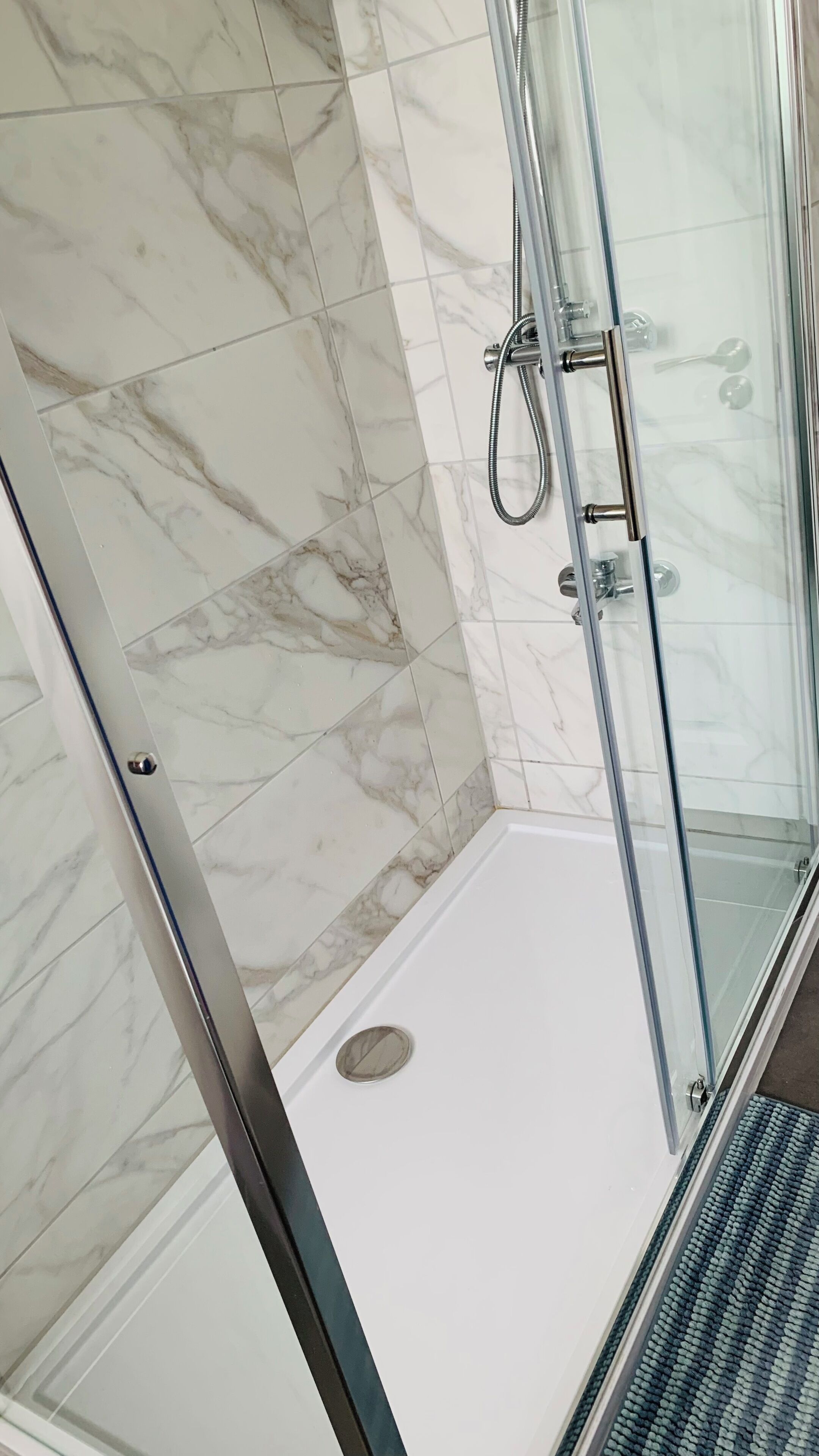 A glass-enclosed shower with a white floor, marble wall tiles, and a metal showerhead.