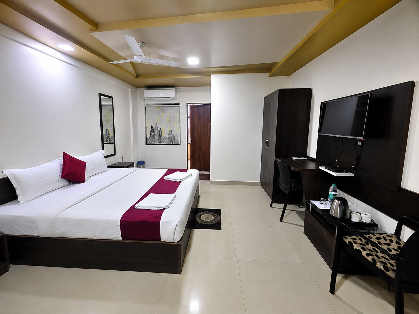 A hotel room with a bed, a desk, a television, and an air conditioning unit.
