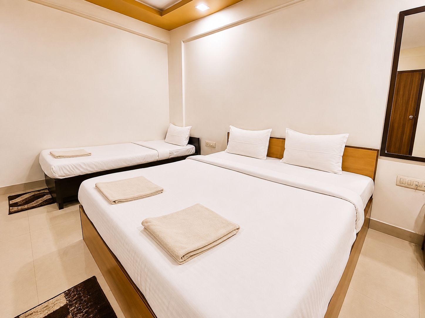 Camera d'albergo con un letto grande, due letti più piccoli, una testiera in legno e uno specchio a parete.