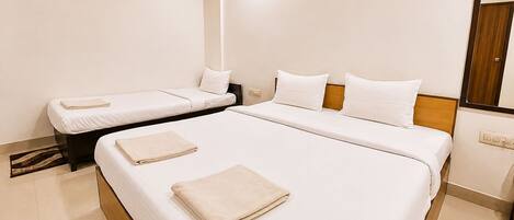 A hotel room with a large bed, two smaller beds, a wooden headboard, and a mirror on the wall.