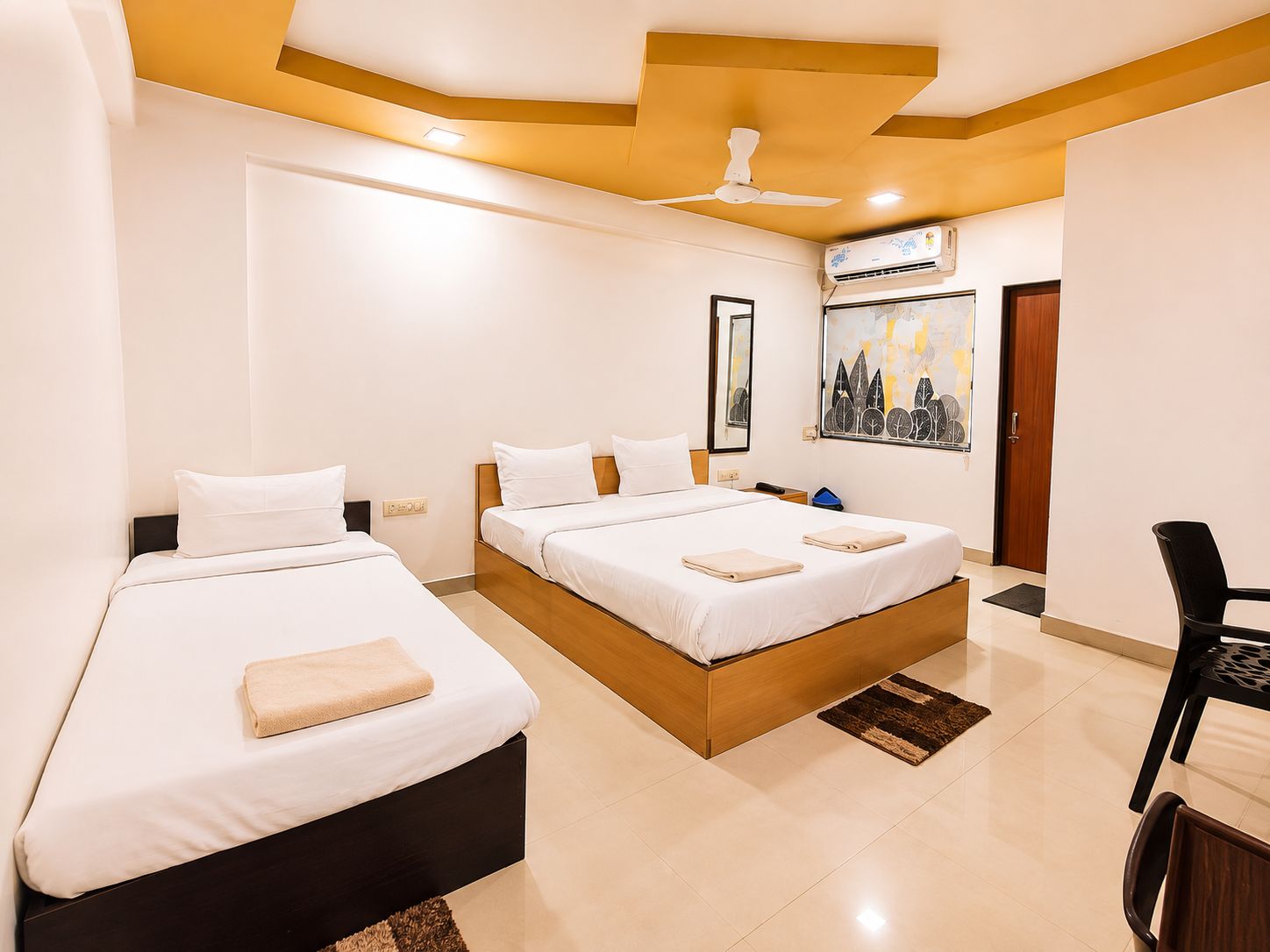 Habitación de hotel con dos camas, ventilador de techo, equipo de aire acondicionado, una obra de arte enmarcada y una puerta.