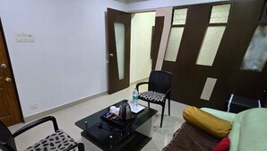 A living room with a sofa, a coffee table, a chair, and a ceiling fan. - Hotel Sukh Sagar (Veraval)