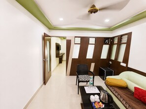 Habitación de hotel con sofá, sillón, mesa de centro y televisor.