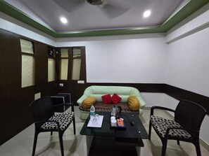 A room with a green sofa, two black chairs, a table with a bottle, glasses, and a cup.