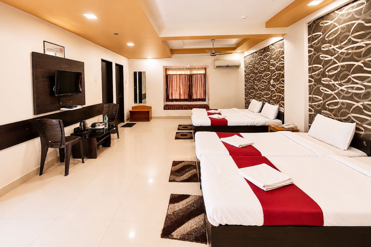 A hotel room with two beds, a desk, a chair, a television, and a ceiling fan.