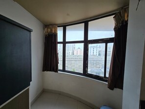 A room with a large window, a blackboard, and a view of buildings outside. - Hotel Sukh Sagar (Veraval)