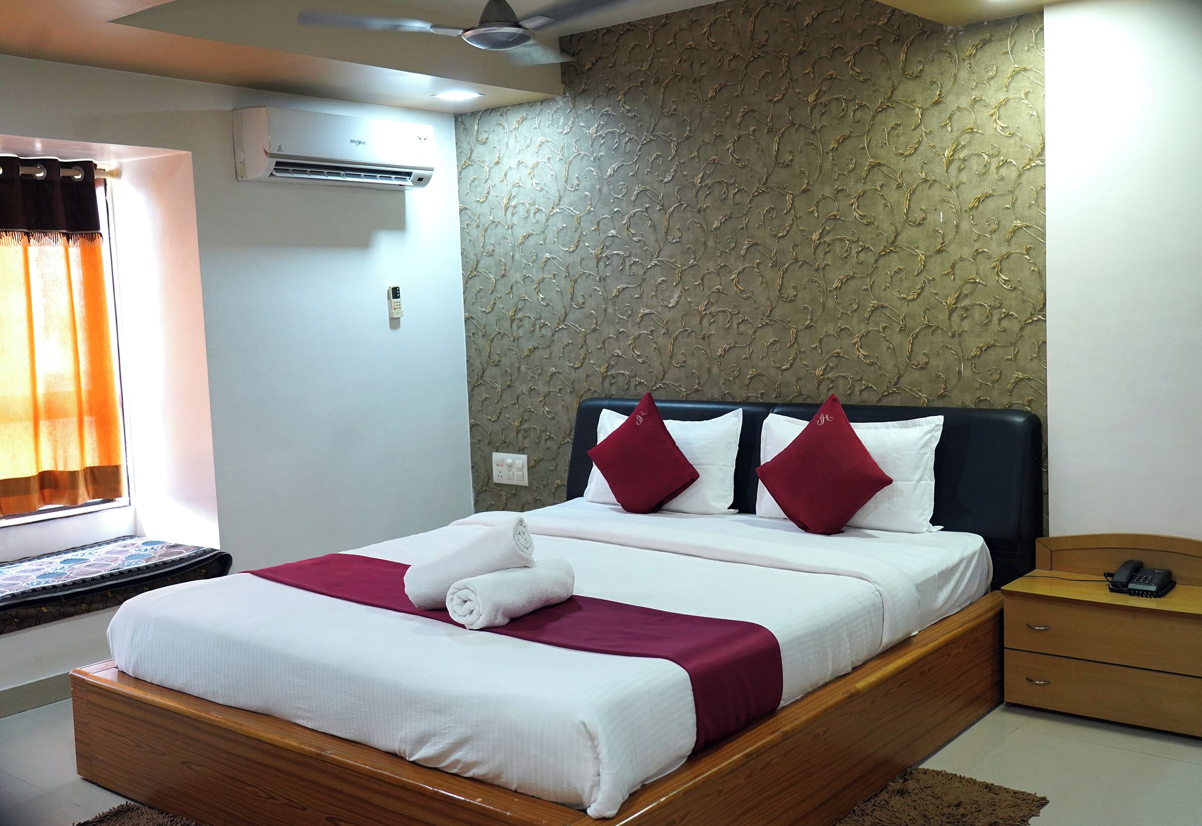 Habitación de hotel con cama, mesita de noche, teléfono y aire acondicionado de pared.