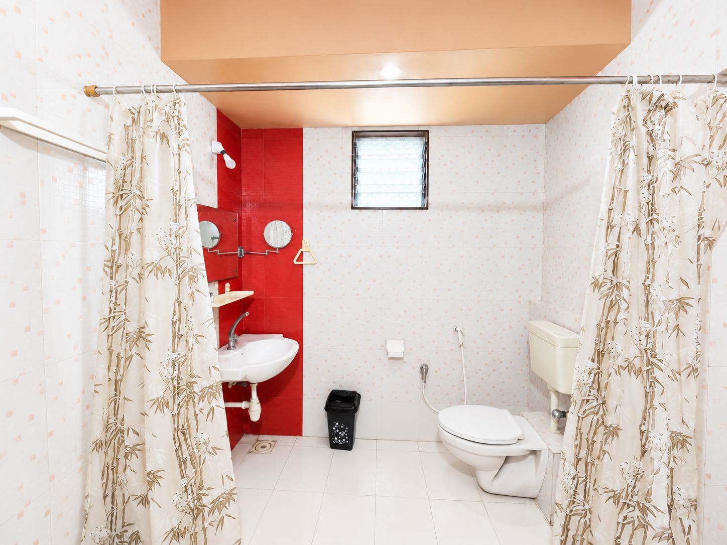A bathroom with a toilet, sink, and shower area, featuring a red accent wall and bamboo-patterned curtains.