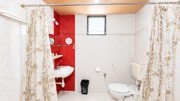 A bathroom with a toilet, sink, and shower area, featuring a red accent wall and bamboo-patterned curtains.