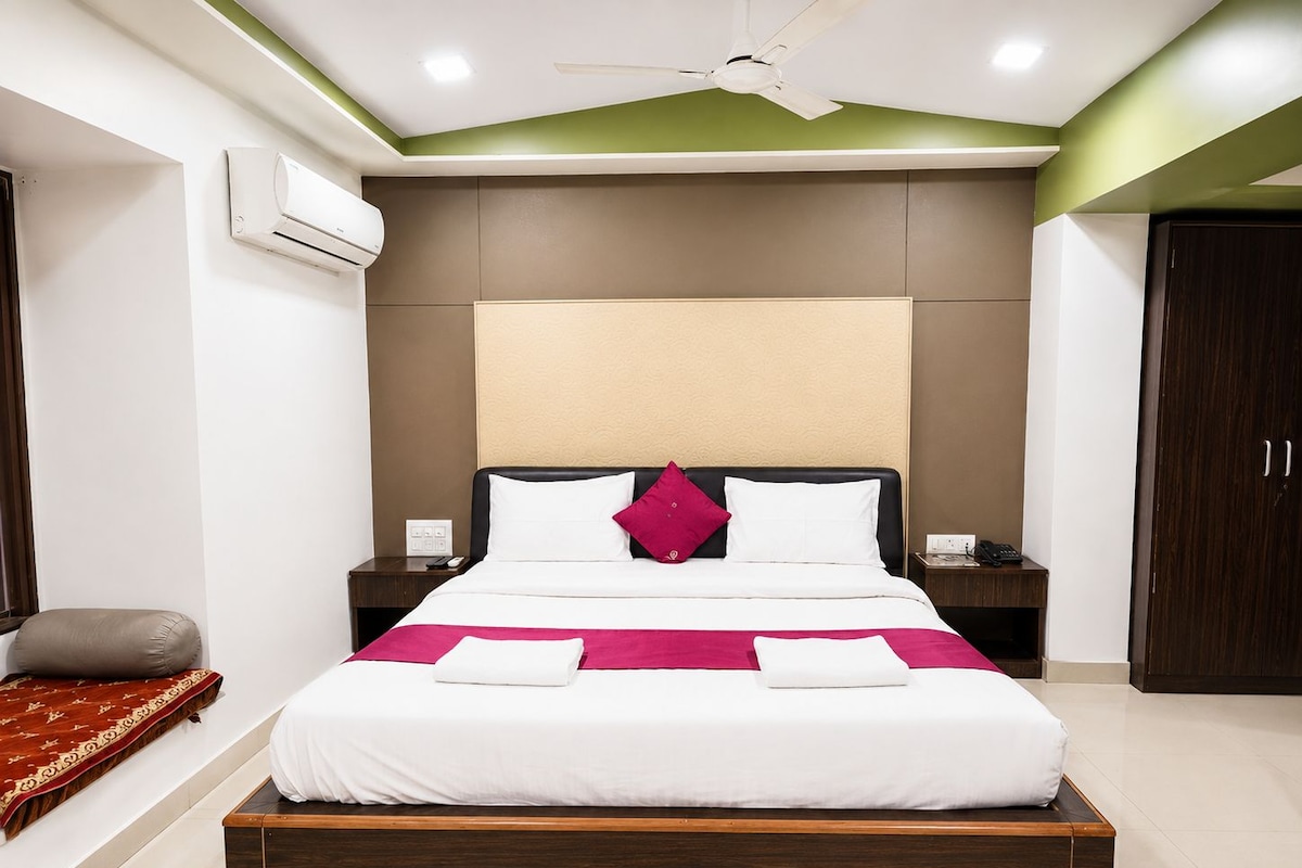 A hotel room with a bed, bedside tables, an air conditioning unit, a ceiling fan, and a wardrobe.