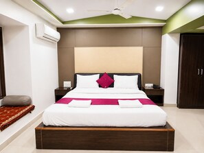 A hotel room with a bed, bedside tables, an air conditioning unit, a ceiling fan, and a wardrobe.