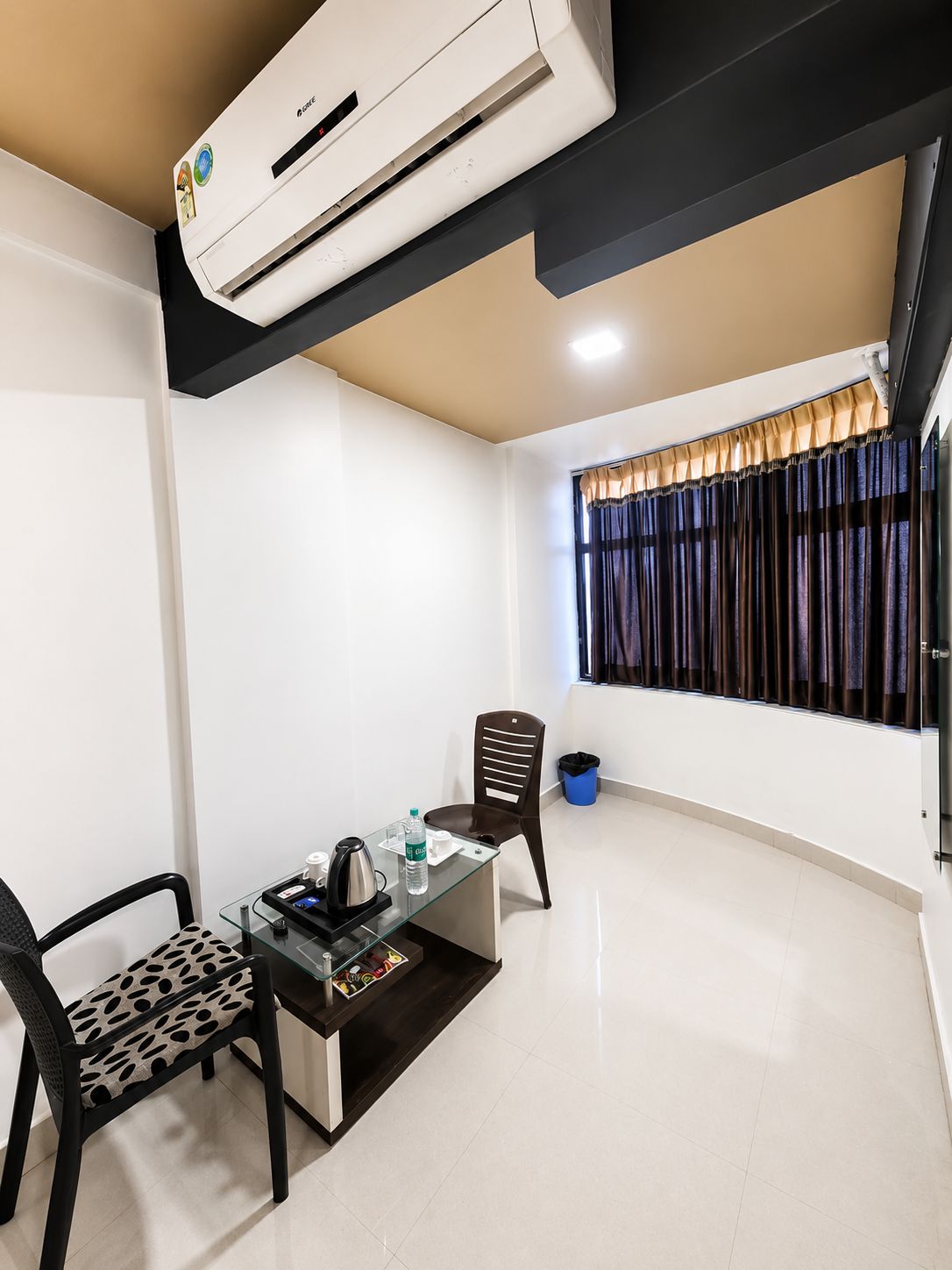 Habitación de hotel con kitchenette, comedor con mesa y sillas, ventana con cortinas y un cesto de basura.