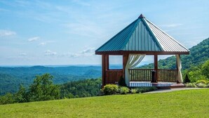 A gazebo with a metal roof and wooden structure, surrounded by a grassy area with a view of distant hills. - 3 Brothers Bears | Smoky Mountain Escape (Sevierville)